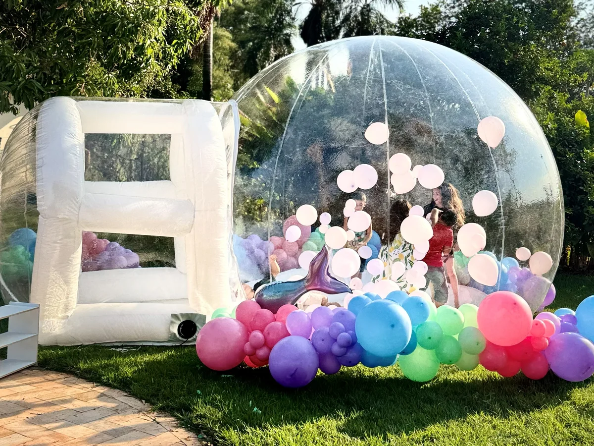 Bubble Dream House — cúpula transparente com balões flutuantes, ligada à antecâmara branca de entrada, montada no gramado